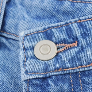 Close-up of metal button on blue denim fabric with detailed orange contrast stitching