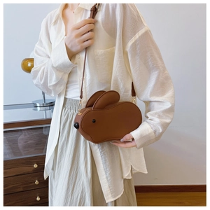 Détail du sac à bandoulière lapin marron avec chaîne dorée sur la tenue du modèle