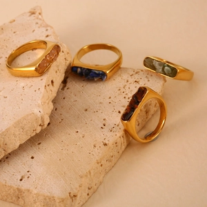 18K Gold Edelstahlringe mit bunten Natursteinen auf strukturiertem Steinuntergrund