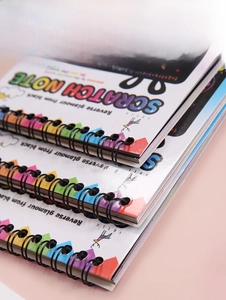 Detailed close-up of three scratch art notebooks with black metal wire-o binding and colorful edges