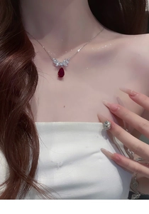 Close-up of a silver necklace with red teardrop zircon pendant worn on a female neck