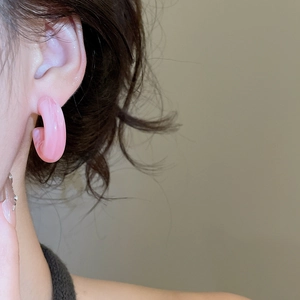 Close-up of a pink translucent C-shape resin hoop earring worn by a female model