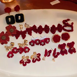 Elegant red velvet floral earrings set with gold plating and pearls on a white plate