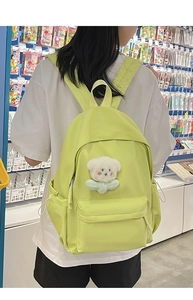 Light green casual fabric backpack with white plush bear charm shown on model in shop