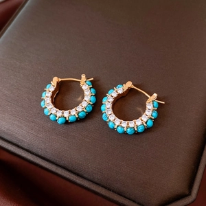 Macro shot of gold plated earrings with sky blue turquoise and white cubic zirconia stones