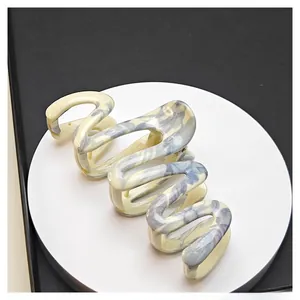 Detail of wave-shaped hair claw with blue ink marble pattern on cream acetate surface