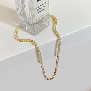 Close-up of golden tennis necklace with sparkling square zircon stones on a white stand