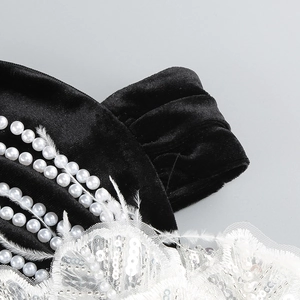 Détail de robe en velours noir avec perles blanches, dentelle pailletée et plumes