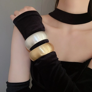 Close-up of matte gold and pearly silver oval wide open bangles on a model's wrist