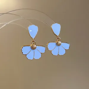 Elegant gold-tone floral earrings with light blue enamel petals on a luxury display stand