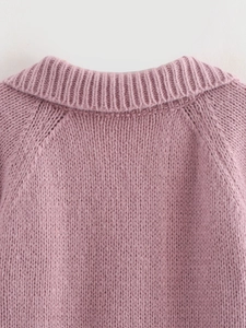 Close-up detail of the pink V-neck knitted sweater showing collar and shoulder texture