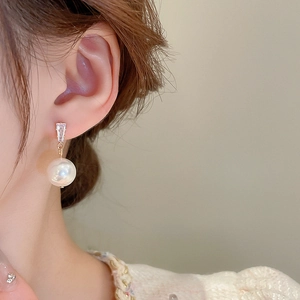 Detailed close-up of a pearl earring with a rectangular zircon on a model's ear