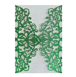 Intricate laser-cut green glitter invitation cover with symmetrical scrollwork patterns
