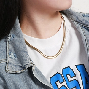 Detailed close-up of a wide gold flat snake chain necklace on a model's neck