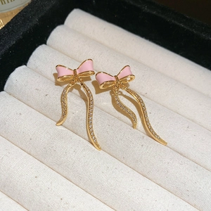 Macro shot of sweet pink bow earrings with sparkling golden tassels on beige canvas