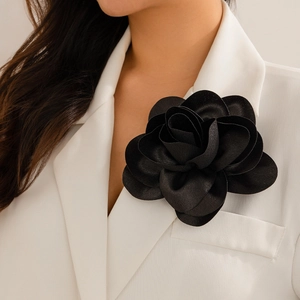 Detail of a large black rose brooch with layered fabric petals worn on a white blazer lapel