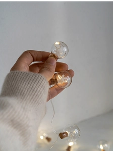 Detail of warm LED glass ornament string light with snowflake inside held by hand