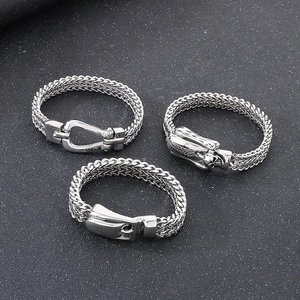 Detail view of three stainless steel braided rings with skull, U-shape, and belt buckle clasps