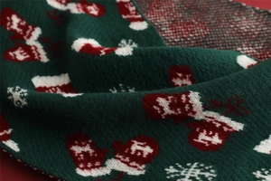 Close-up of dark green knitted Christmas scarf featuring red stocking and snowflake patterns