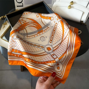 Classic orange silk scarf with equestrian chain print displayed on a black tray