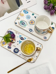 Detail of ceramic Evil Eye coffee set including two mugs, gold spoon, and tray