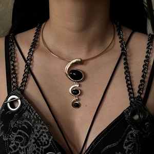 Close-up of gold metal choker featuring a spiral of three black resin oval pendants