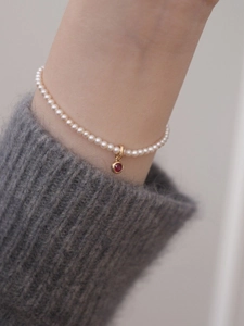 Macro shot of pearl bracelet with gold pendant featuring a vibrant red zircon stone