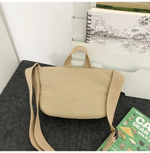 Minimalist beige nylon crossbody bag placed on a grey felt desk for daily commuting