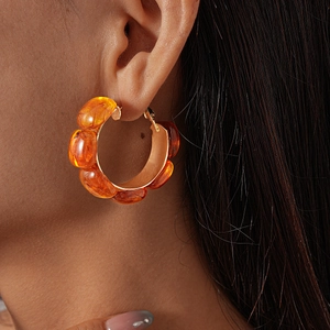 Close-up of amber resin geometric hoop earrings with polished gold-tone metal frame