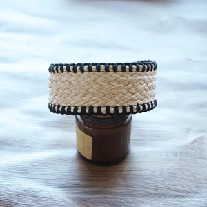 Detail of handwoven beige raffia headband featuring contrast black stitched edges on wood