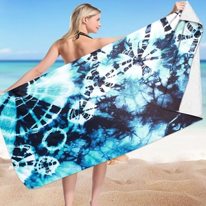 Blue tie-dye microfiber beach towel held by a model on a sunny seaside beach