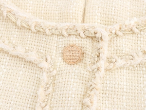 Dettaglio macro del tessuto tweed beige con bordo intrecciato dorato e bottone dorato
