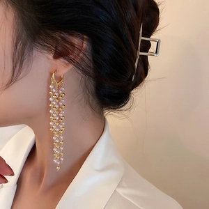 Elegante goldfarbene Herz- und Perlen-Quasten-Ohrringe getragen für einen schicken Look