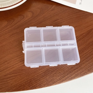 Macro shot of 6-grid transparent plastic jewelry storage box on a wooden desk