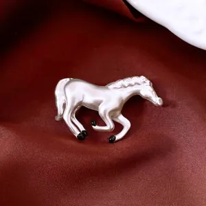 Silver horse brooch with black enamel accents on dark red satin background luxury fashion
