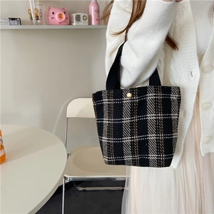 Close-up of a checkered wool bento bag with a black handle and stylish metal clasp