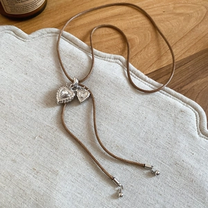 Detailed macro view of a silver double heart pendant with zircon on a brown woven cord