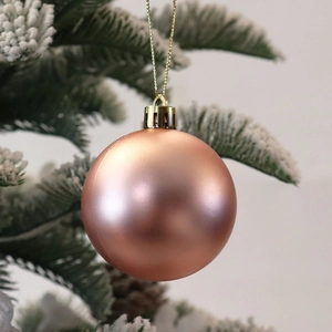 Rose gold Christmas ball ornament hanging on snowy pine branch for festive tree decor
