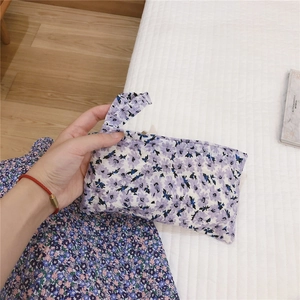 Vue détaillée d'une pochette en tissu à fleurs mauves tenue à la main sur fond cosy