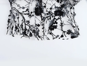 Detail of floral flocking on sheer mesh fabric with black branch pattern and hem finish