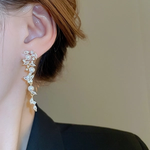 Detail shot of long pearl earrings with leaf-shaped zircon settings on a gold-plated base