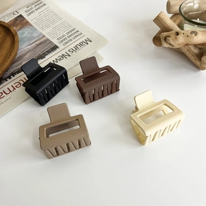 Matte square hair claw clips in four neutral earth tones displayed on a wooden base