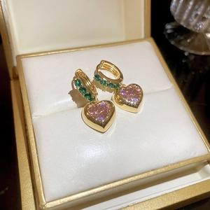Macro shot of gold hoop earrings with green stones and pink heart zircon pendants