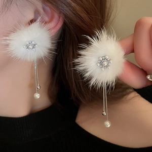Close-up of white plush ball earrings with pearl accents and hanging metal tassels