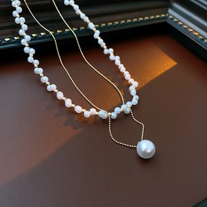 Detail of double-layer pearl necklace with gold chain on dark leather surface