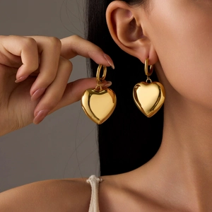 Détail de boucles d'oreilles pendantes cœur en or 18K avec finition polie portées par un mannequin