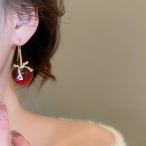 Dettaglio di orecchini a ciliegia rossi con stelo dorato indossati da una modella