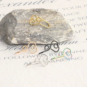 Five colors of stainless steel fake nose rings displayed on a textured stone and paper