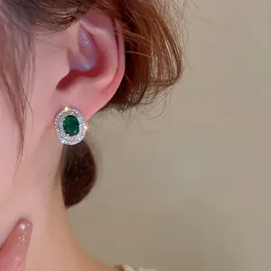 Elegant emerald green stud earrings with sparkling zircon halo on model's ear