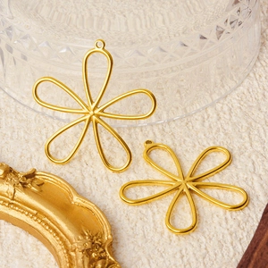 Two golden hollow floral 304 stainless steel pendants on a textured beige fabric backdrop
